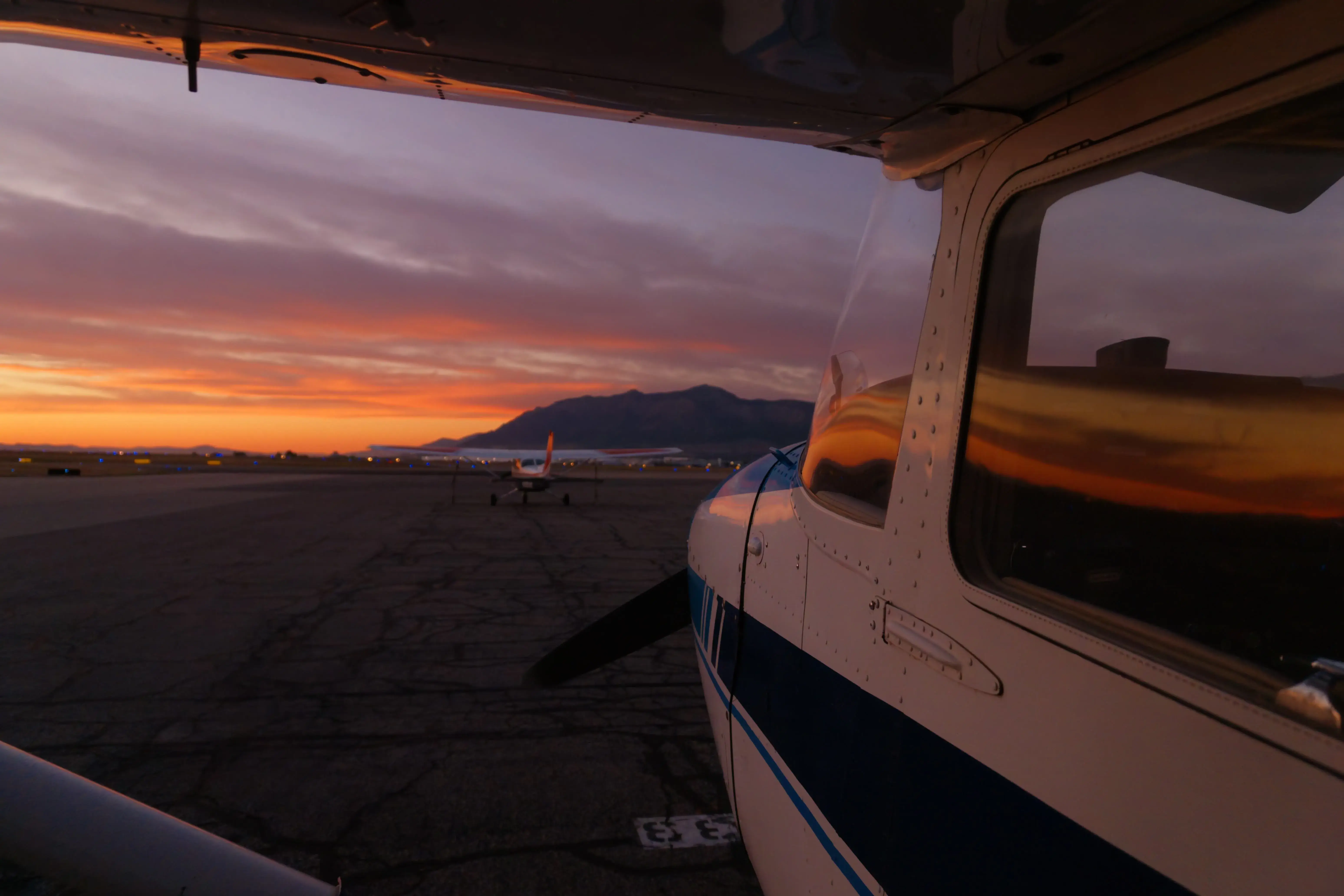 Sunset over the ramp and mountains seen from beside the wing of a Blitz Aviation Cessna