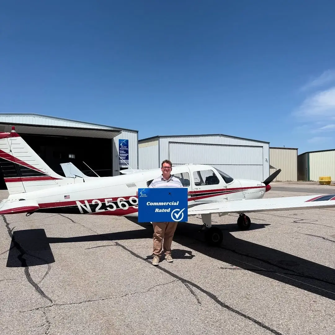 Man in front of an airplane holding a poster with "Commercial Rated" written on it