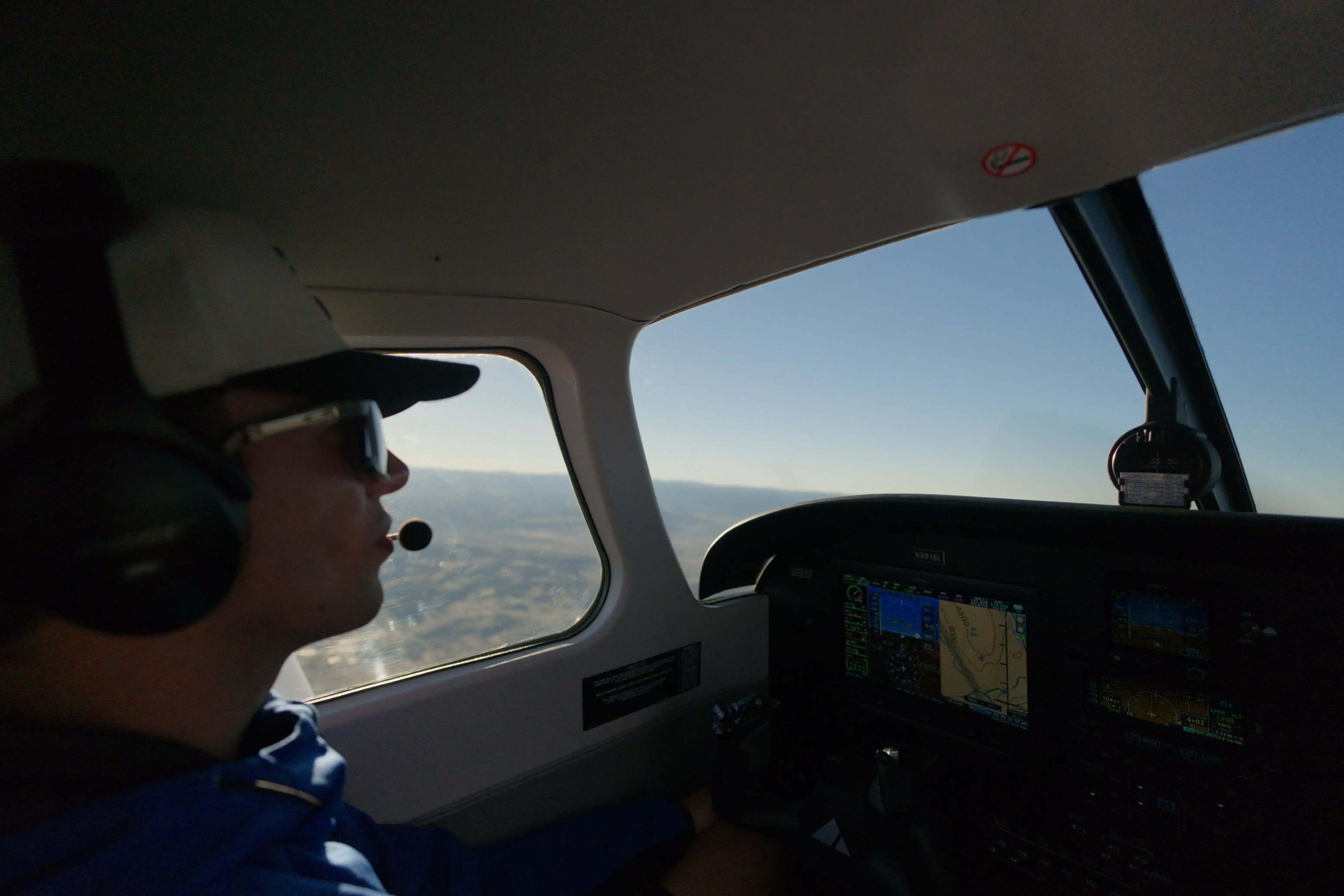 Student pilot wearing a headset flying a glass cockpit Piper over open terrain