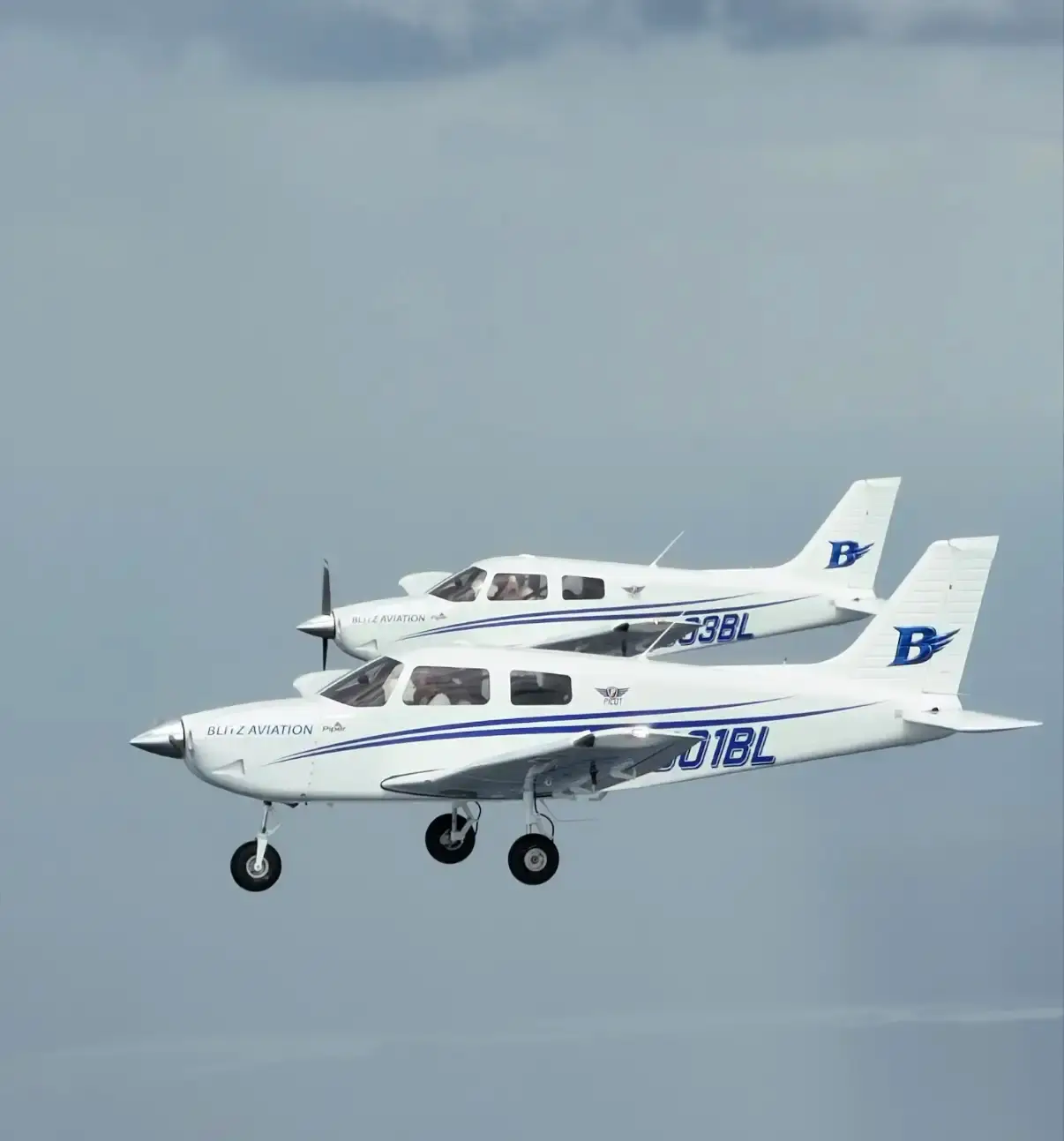Two Blitz Aviation Piper Pilot 100i airplanes flying in formation with the winged B logo on their tails